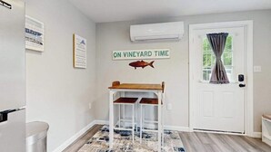 Una stanza con una porta bianca, un tavolino con una decorazione a forma di pesce, un condizionatore d'aria a parete e un cartello con su scritto 'ON VINEYARD TIME'.