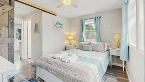 Una camera da letto con un letto, comodini, una ventola a soffitto, una finestra con tende e una porta che dà su un'altra stanza.