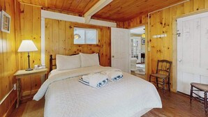 Ein Zimmer mit Holzwänden, einem Bett, einem Nachttisch, einem Sessel und einer Tür.