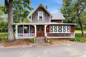 A two-story house with a porch, a front door, and a window. - Charming home with walkable beach, large yard, deck, fire pit, and A/C (Oak Bluffs)
