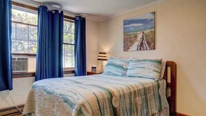 Ein Schlafzimmer mit Bett, einem Fenster mit Vorhängen, einer Lampe und einem Bild an der Wand.