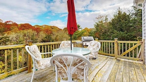 Une terrasse en bois avec une table et des chaises en verre, un parasol rouge et un barbecue.