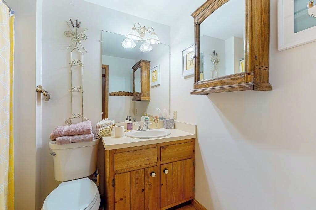 A bathroom with a toilet, sink, wooden cabinet, and a mirror.