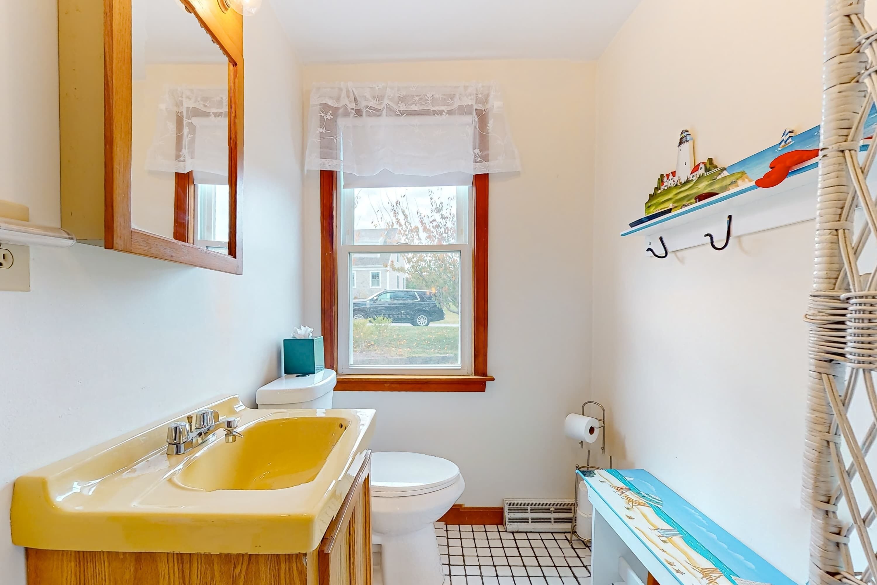 Une salle de bain avec un lavabo jaune, des toilettes blanches et une fenêtre donnant sur une maison.
