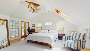 A bedroom with a large bed, a chair, a desk, and a chandelier. - Quiet home near Pilgrim Lake with deck, W/D, AC, games, & large yard (Orleans)