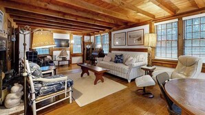 A cozy living room with wooden beams, a sofa, a chair, a table, and a fireplace. - Quiet home near Pilgrim Lake with deck, W/D, AC, games, & large yard (Orleans)