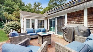 A covered outdoor patio with wicker furniture, a barbecue grill, and a glass door leading to a covered area. - Quiet home near Pilgrim Lake with deck, W/D, AC, games, & large yard (Orleans)