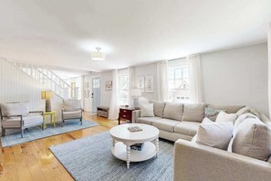Ein Wohnzimmer mit Sofa, zwei Sesseln, einem Couchtisch, einer Lampe und einer Treppe.