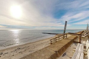 A beach with a wooden walkway leading to the water, a signpost, and a row of benches.