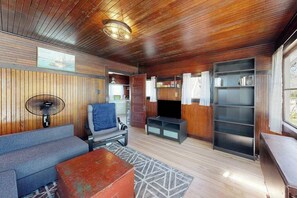 A room with wooden walls, a sofa, a television, and a bookshelf.