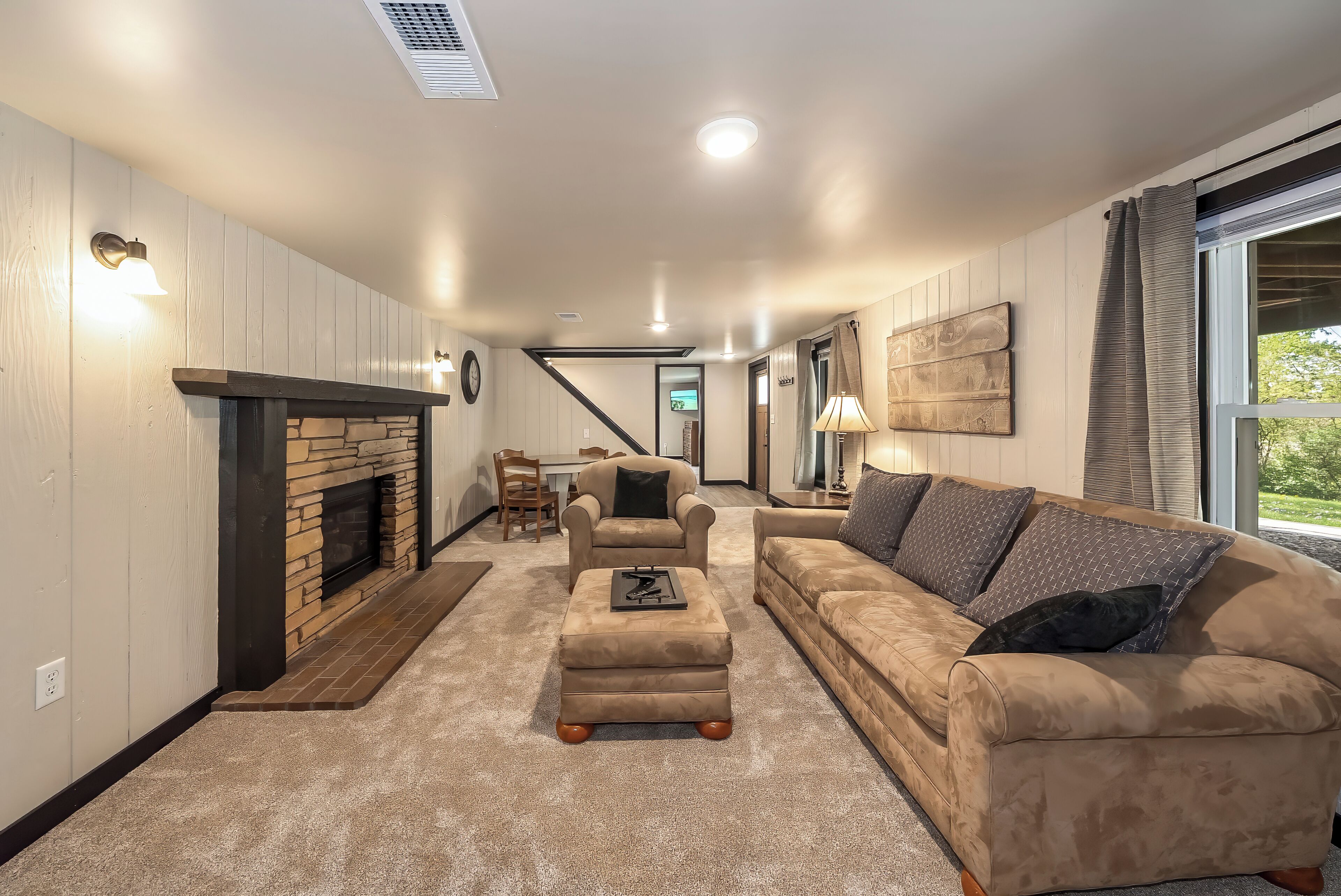 A living room with a fireplace, a sofa, an ottoman, and a dining area in the background.