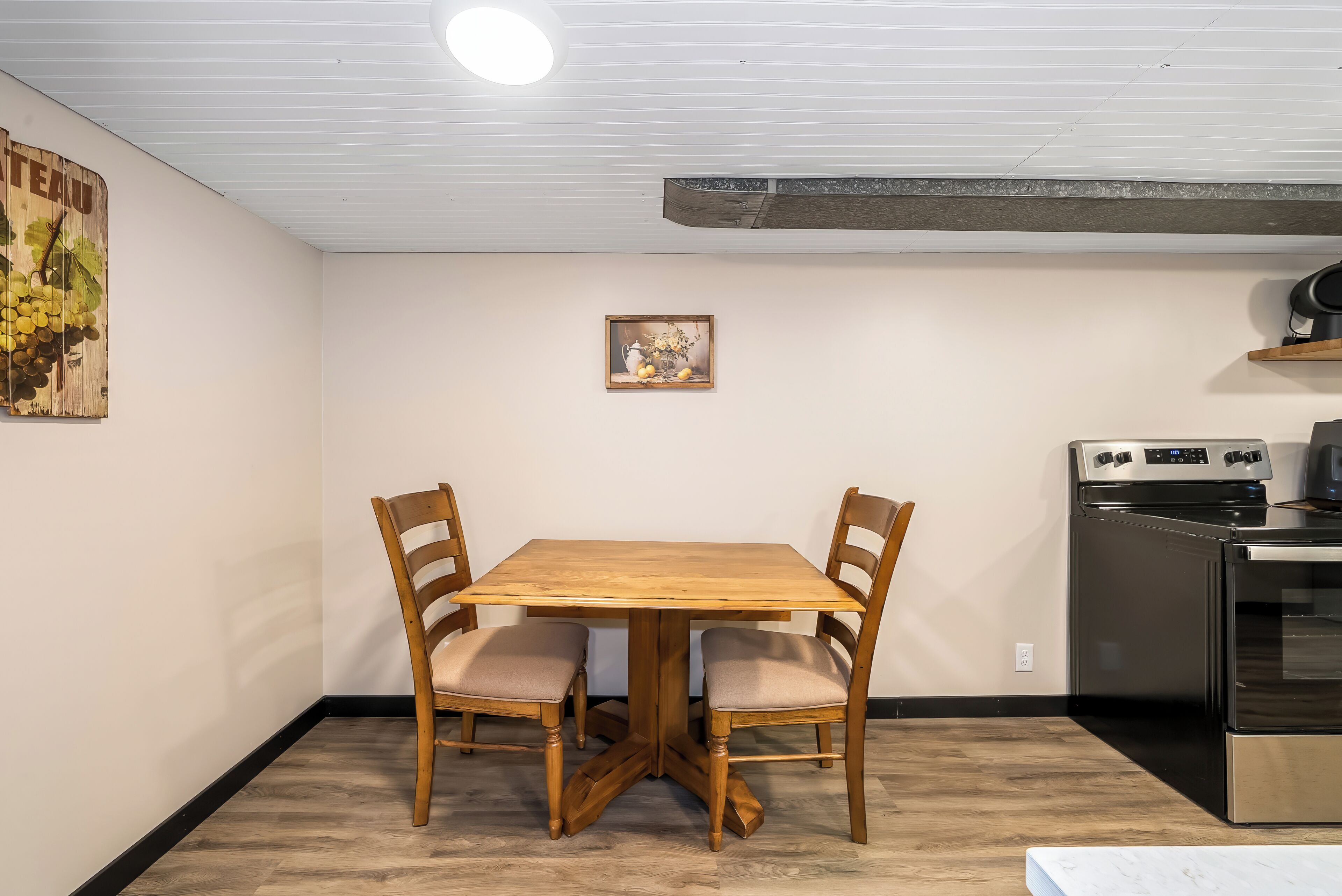 A dining table with four chairs, a kitchen with a stove, and a wall-mounted picture.