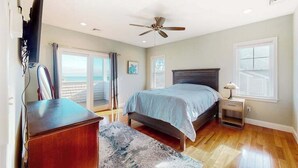 Ein Schlafzimmer mit einem Bett, einem Schreibtisch, einem Stuhl, einem Deckenventilator und einem Fenster.