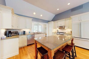 A kitchen with white cabinets, a granite countertop island, and wooden stools. - Spacious home with huge deck & tree-lined yard, grill, & WiFi - great location (Orleans)