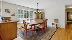 Un espace repas avec une table et des chaises en bois, un lustre et une vue dégagée grâce à de grandes fenêtres.