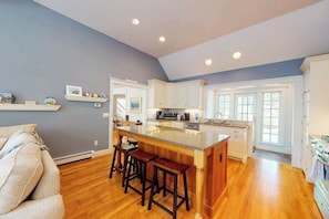 A kitchen with a central island, wooden bar stools, white cabinets, and a grey wall. - Spacious home with huge deck & tree-lined yard, grill, & WiFi - great location (Orleans)