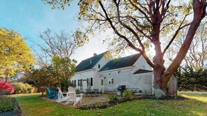 Ein zweigeschossiges Haus mit einem großen Baum im Vorgarten, einer Terrasse mit Gartenmöbeln und einem Gerätehaus.