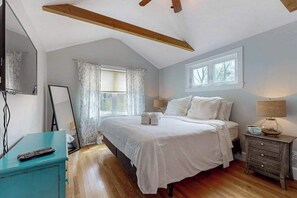 Ein Schlafzimmer mit Bett, Nachttisch, Spiegel, Fenster und Deckenventilator.