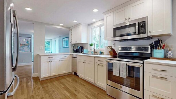 A modern kitchen with white cabinets, stainless steel appliances, and a wooden floor. - Skaket Beach escape: Corner-lot home with big yard - walk to Warm Bayside Shore (Orleans)