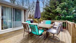 A wooden deck with outdoor furniture, including a table and chairs, and a covered umbrella. - Skaket Beach escape: Corner-lot home with big yard - walk to Warm Bayside Shore (Orleans)