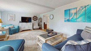 A living room with a sofa, coffee table, TV, and artwork on the wall. - Skaket Beach escape: Corner-lot home with big yard - walk to Warm Bayside Shore (Orleans)