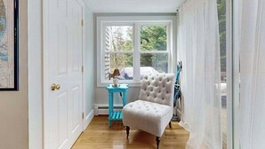 A hallway with a white door, a window with a view of trees, a blue side table, and a white chair. - Skaket Beach escape: Corner-lot home with big yard - walk to Warm Bayside Shore (Orleans)