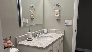 Et badeværelse med et hvidt toilet, en granitvask, et spejl med lys og et håndklædestativ.