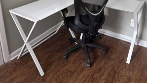 Et hjørnekontor med et hvidt skrivebord, en sort kontorstol og et vindue med persienner.