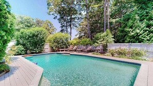 Une piscine rectangulaire à l’eau claire, entourée d’une terrasse en bois et d’une végétation luxuriante.