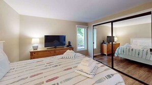 Ein Schlafzimmer mit Bett, Fernseher, Kommode und einer Schiebetür zu einem anderen Raum.