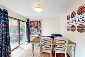 A dining area with a wooden table, white chairs, and a view through a glass door to an outdoor patio.
