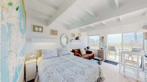 A bedroom with a large bed, a desk, and a chair. There is a map on the wall and a view of the outdoors through the window. - Ocean-view studio near golf with patio, beach gear, kitchenette, & partial AC (North Truro)