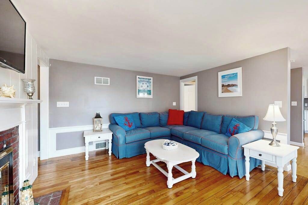A living room with a blue sectional sofa, a white coffee table, a fireplace, and a TV mounted on the wall.