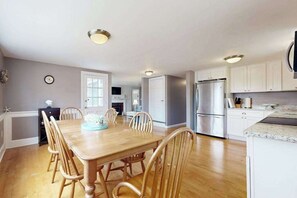 Une cuisine moderne avec des meubles blancs, un réfrigérateur en acier inoxydable et une table à manger en bois, assortie de chaises.