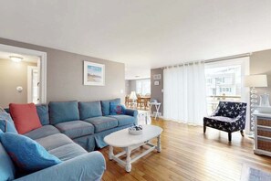 A living room with a blue sofa, a white coffee table, and a patterned armchair. - Renovated, river view home with yard games - walk to town dock & beach (West Dennis)