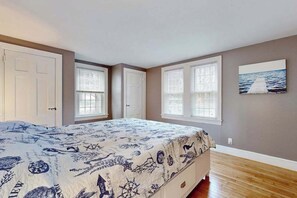 A bedroom with a bed, two windows, a door, and a painting on the wall. - Renovated, river view home with yard games - walk to town dock & beach (West Dennis)
