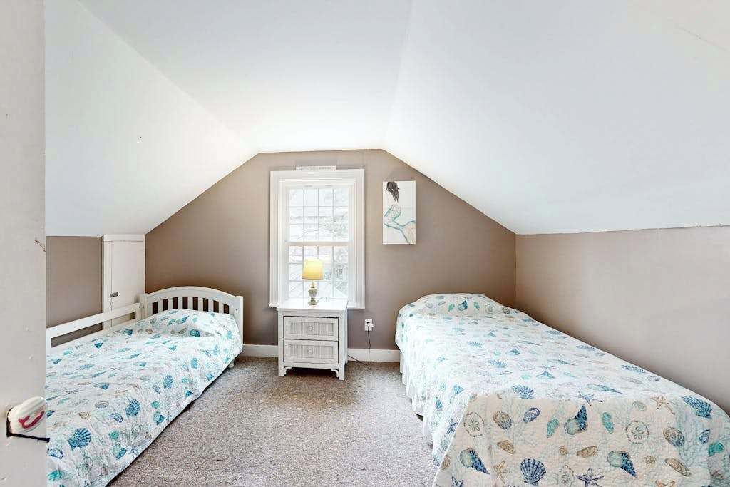 Ein Schlafzimmer mit zwei Einzelbetten, einem Nachttisch mit Lampe, einem Fenster und einem Wandbild.