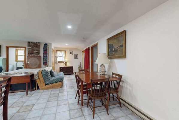 A room with a dining table, chairs, a sofa, a lamp, and a painting on the wall.