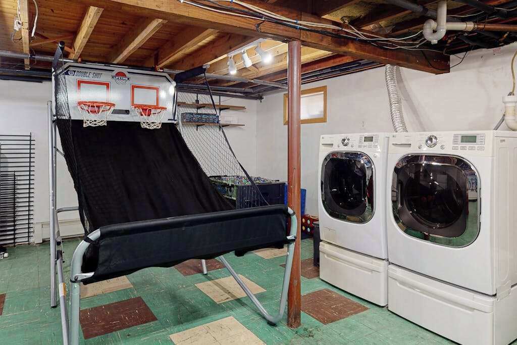 A laundry room with a washing machine and dryer, a metal rack, and a ceiling with exposed beams.