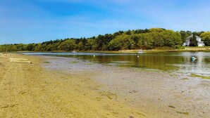 A beach with a house on a hill, calm water, and boats.