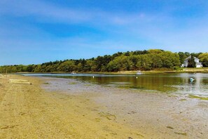 A beach with a house on a hill, calm water, and boats.