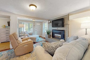 A living room with a fireplace, a sofa, a recliner, and a TV mounted on the wall.