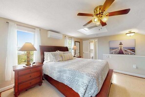 A bedroom with a bed, nightstand, lamp, ceiling fan, and a painting on the wall.