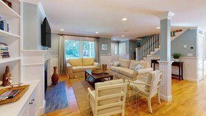 A spacious living room with a sofa set, a coffee table, and a bookshelf. - Gorgeously rebuilt Cape Cod estate with lovely grounds, walk to private beach (West Yarmouth)