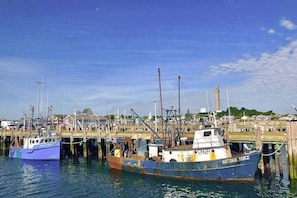 Ein Hafen mit an Holzstegen liegenden Booten, einem klaren Himmel und einem Gebäude in der Ferne.