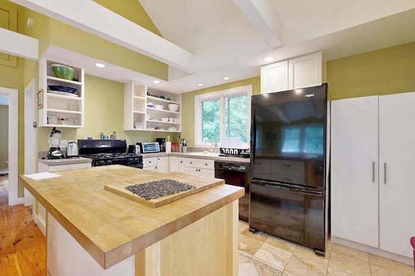 A modern kitchen with a central island, built-in shelves, a large refrigerator, and a window providing natural light.