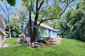 A house with a blue exterior, a front yard with a tree, and a small wooden structure.