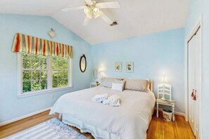 Ein Schlafzimmer mit Bett, Fenster, Deckenventilator, Nachttisch und Sessel.