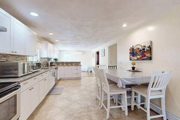 A modern kitchen with white cabinets, a dining table with chairs, and a painting on the wall.
