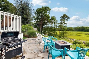 Un patio con una parrilla, mobiliario exterior y vista a un campo verde.